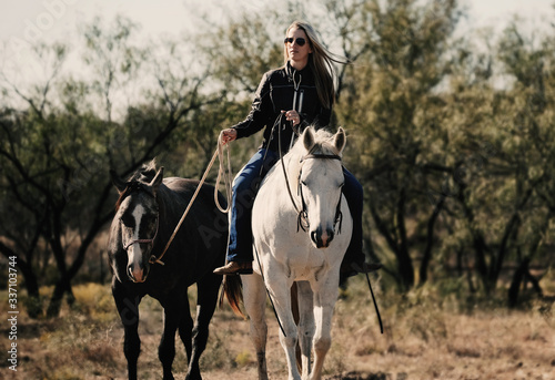 Western lifestyle image of woman riding horse and ponying on rural farm.