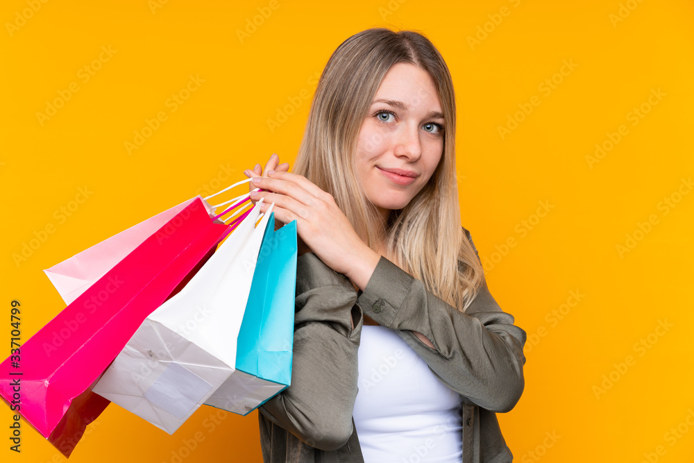 Young blonde woman over isolated yellow background holding shopping bags