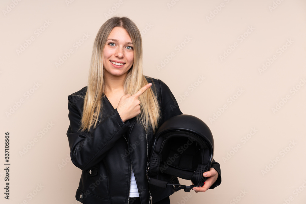 Young blonde woman with a motorcycle helmet over isolated background pointing finger to the side Young blonde woman with a motorcycle helmet over isolated background pointing finger to the side