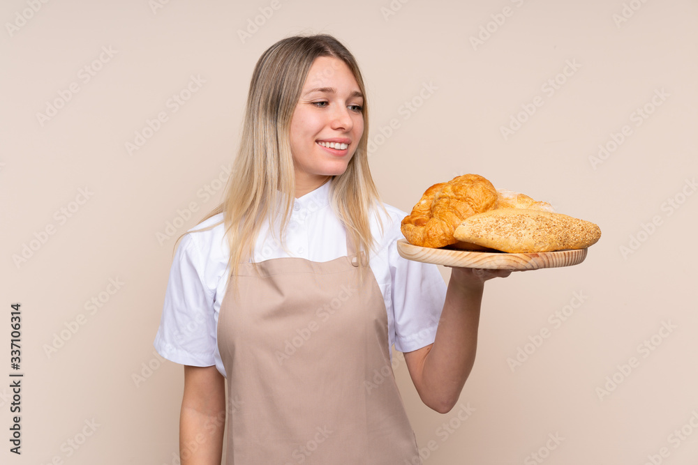 Young blonde girl with apron. Female baker holding a table with several breads with happy expression Young blonde girl with apron. Female baker holding a table with several breads with happy expression