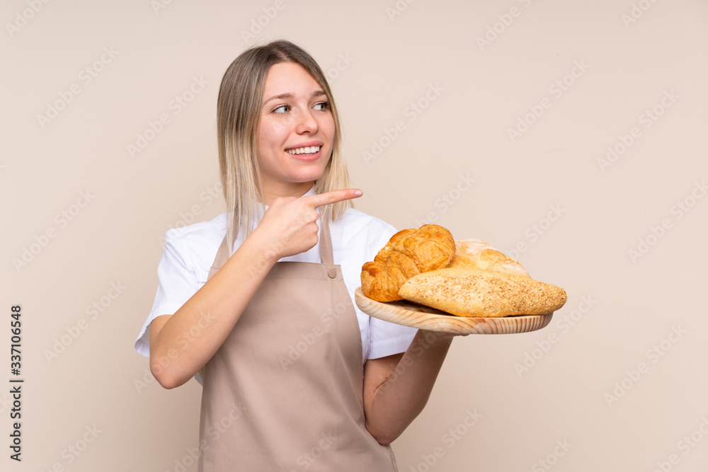 Young blonde girl with apron. Female baker holding a table with several breads pointing to the side to present a product