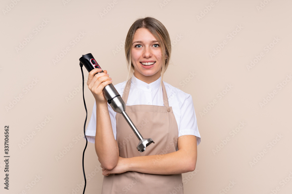 Young blonde woman using hand blender smiling a lot Young blonde woman using hand blender smiling a lot