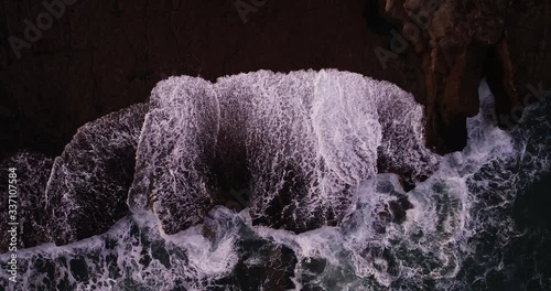 Overhead aerial, waves crash on United Kingdom coastline