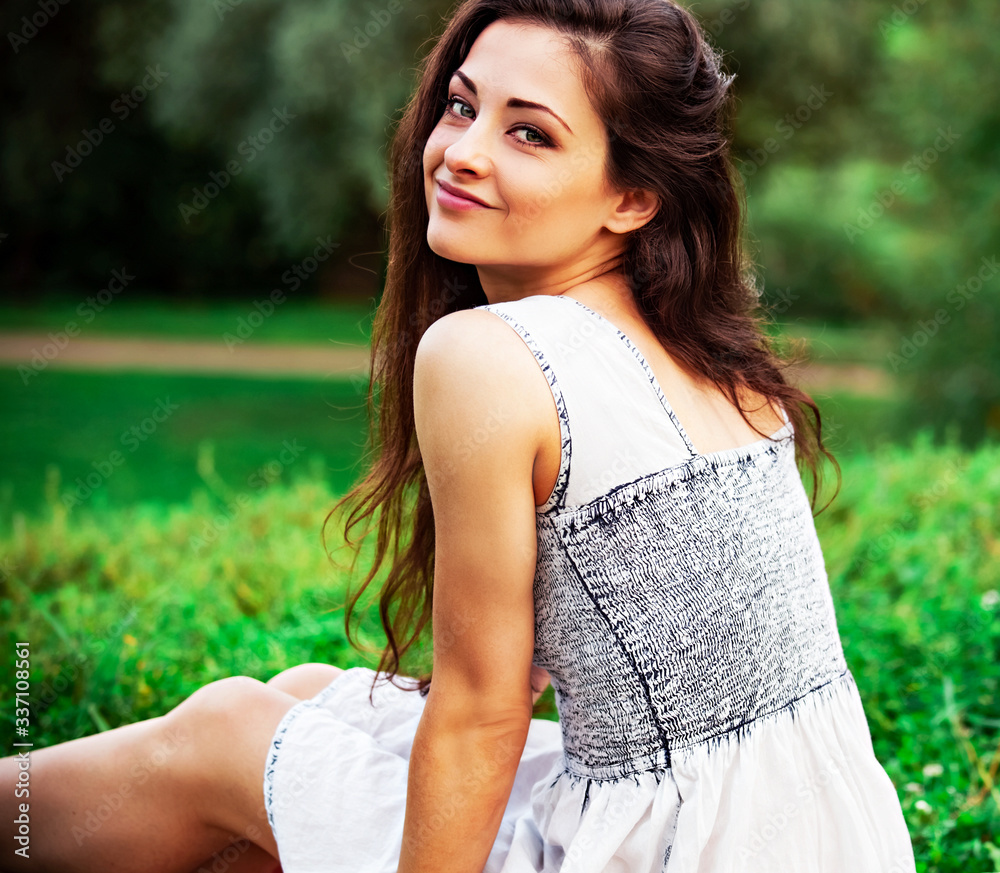 Beautiful happy smiling young woman with long hair sitting on the grass and looking up on summer green background. Closeup Beautiful happy smiling young woman with long hair sitting on the grass and looking up on summer green background. Closeup