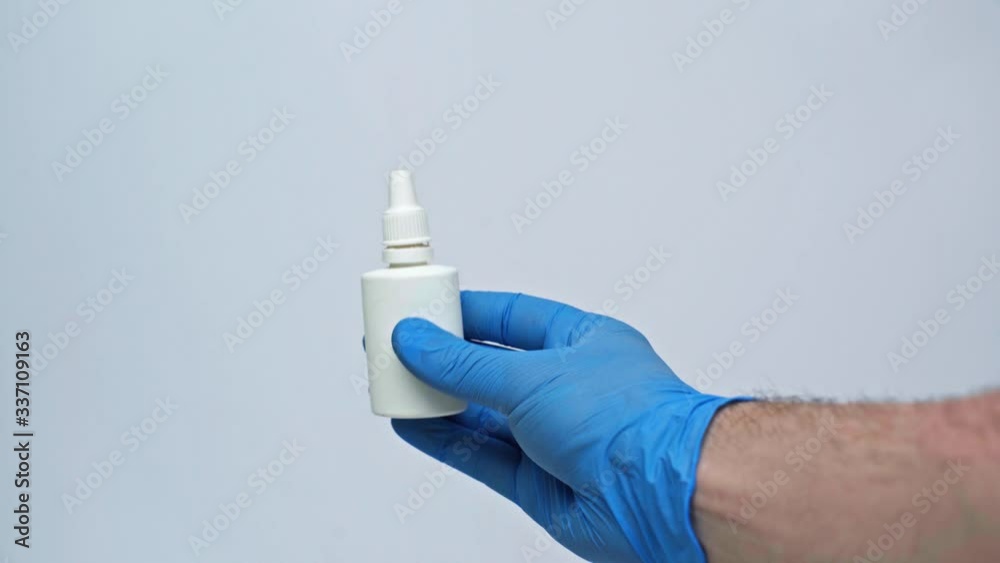 A man’s hand in a blue medical glove holds in his hand a medication for the treatment of the common cold during quarantine. Isolated on a gray background in the studio. The concept of coronavirus. A man’s hand in a blue medical glove holds in his hand a medication for the treatment of the common cold during quarantine. Isolated on a gray background in the studio. The concept of coronavirus.