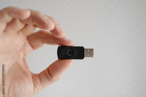 man holds usb flash drive in his hand with his fingertips on a white background