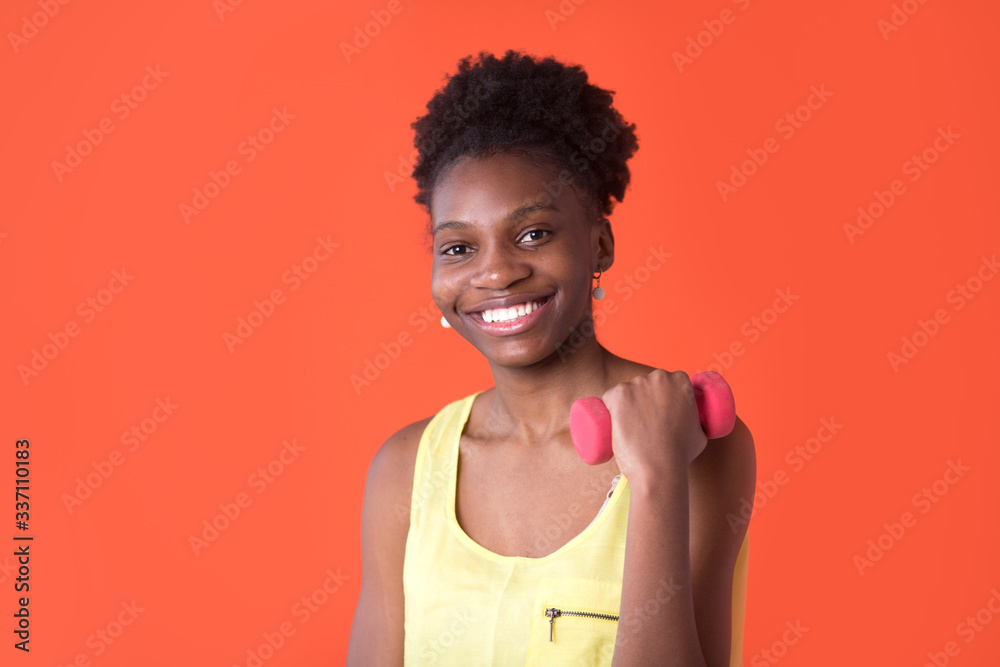 beautiful young african woman on a red background in a yellow t-shirt with dumbbells beautiful young african woman on a red background in a yellow t-shirt with dumbbells