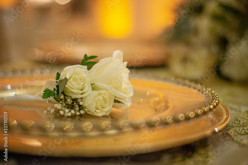 Three white roses on gold charger plate on green table against warm yellow  serene backgound