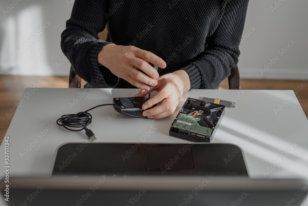 Fototapeta premium repairman repairing a computer mouse in a workshop at a white table. He unscrews the screws with a screwdriver