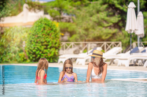 Mother and two kids enjoying summer vacation in luxury swimming pool