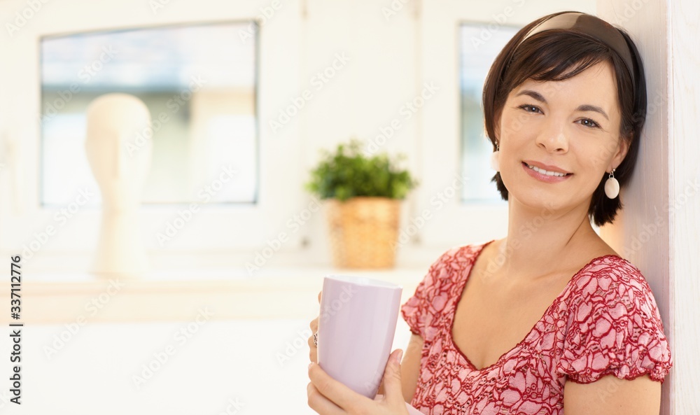 Portrait of young woman at home holding morning coffee cup, looking away, smiling. Portrait of young woman at home holding morning coffee cup, looking away, smiling.