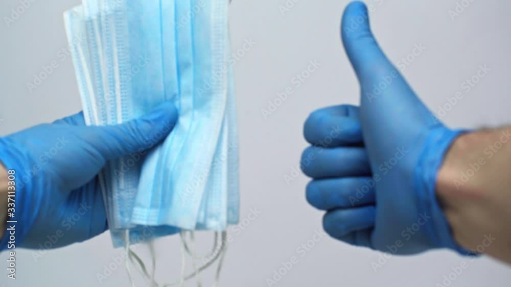 Male hands in blue medical gloves show protective masks and that they are positive for protection during the  coronavirus.Holds thumb up.Isolated on a gray background in the studio.Coronavirus concept