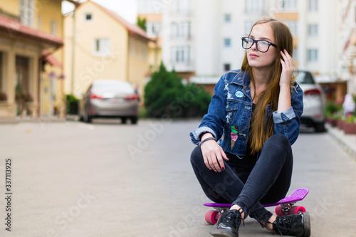Happy attractive young woman sitting on skateboard on the street.