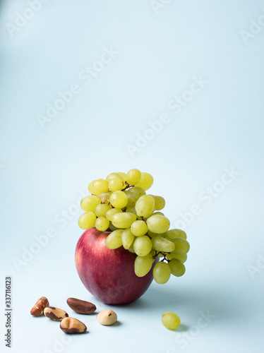 Branch of green grape lies on big red apple wih nuts on blue background