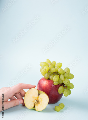 Branch of green grape lies on big red apple wih hand on blue background