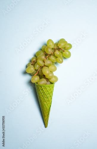 green waffle cone with green grape on light blue background