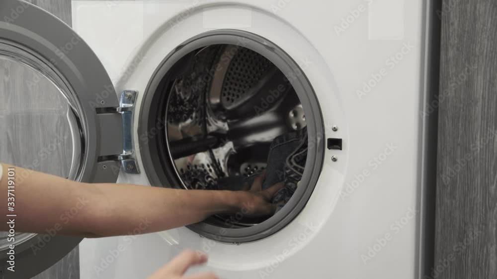 Female hand with married ring put JEANS in laundry machine. Loading washing machine. Load clothes to washer machine. Load clothes laundry washing machine. Preparing laundry washing Female hand with married ring put JEANS in laundry machine. Loading washing machine. Load clothes to washer machine. Load clothes laundry washing machine. Preparing laundry washing