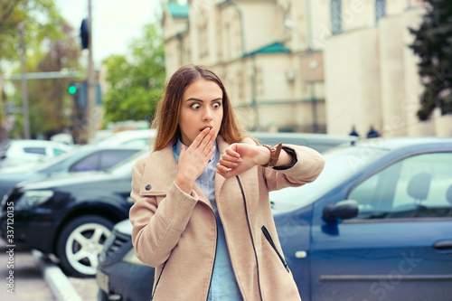 Woman being late to a rendez-vous. Closeup portrait headshot view stressed young attractive beautiful businesswoman checking the time outdoor isolated city scape outdoor background near dealership