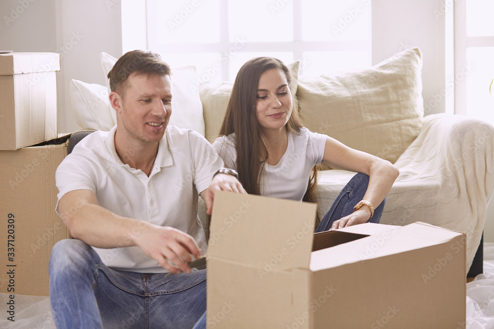 Portrait of happy couple looking at laptop computer together sitting in new house, surrounded with boxes Portrait of happy couple looking at laptop computer together sitting in new house, surrounded with boxes