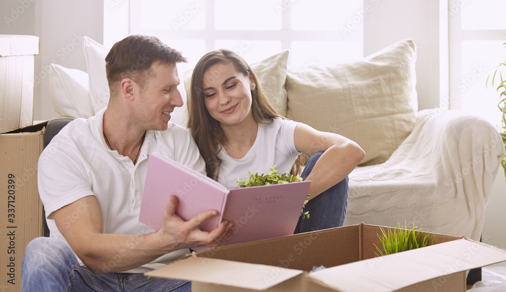 Portrait of happy couple looking at laptop computer together sitting in new house, surrounded with boxes Portrait of happy couple looking at laptop computer together sitting in new house, surrounded with boxes