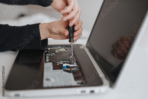 A man disassembles a laptop. Computer service and repair concept. Laptop disassembling in repair shop, close-up. Electronic development, electronic device fixing
