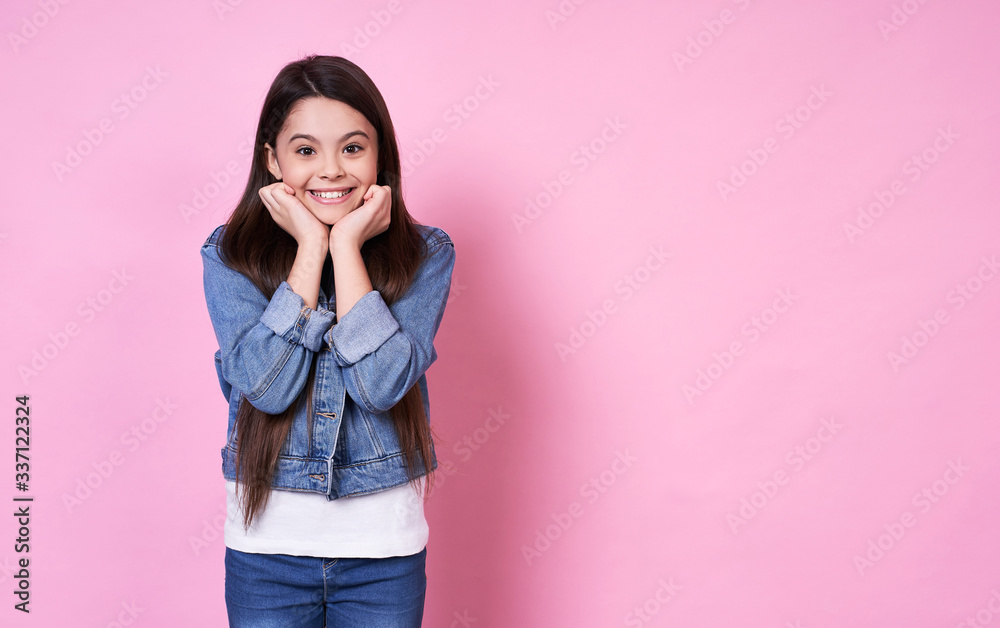 Cute long-haired emotional Caucasian girl in a denim jacket on a pink background.