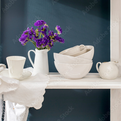 Wallpaper Mural A bouquet of limonium and a set of white dishes: porcelain milk jug, coffee cup, bowls on a white rack on a dark blue background Torontodigital.ca