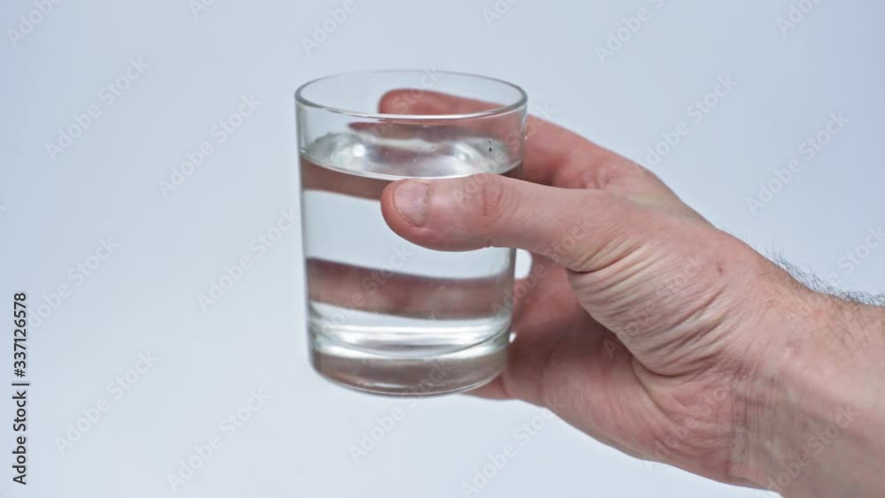 The male hand holds a glass of clean water to drink medicine to protect against coronavirus during quarantine. Isolated on a gray background in the studio. Coronavirus concept The male hand holds a glass of clean water to drink medicine to protect against coronavirus during quarantine. Isolated on a gray background in the studio. Coronavirus concept