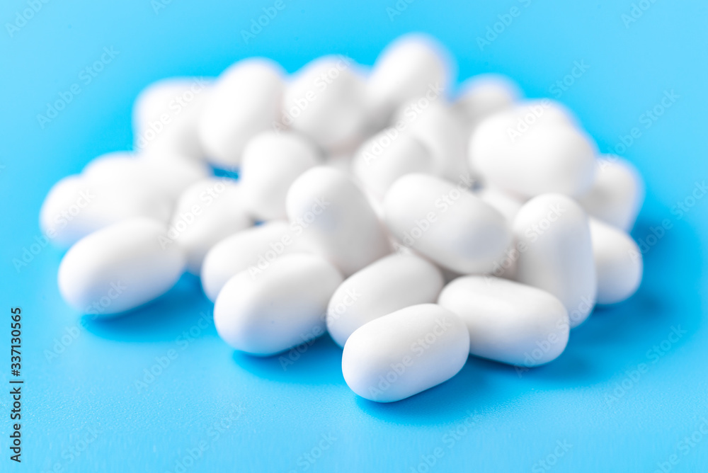 White dragees lie in a pile on a blue background. Close-up, macro photography. Lots of white mints White dragees lie in a pile on a blue background. Close-up, macro photography. Lots of white mints
