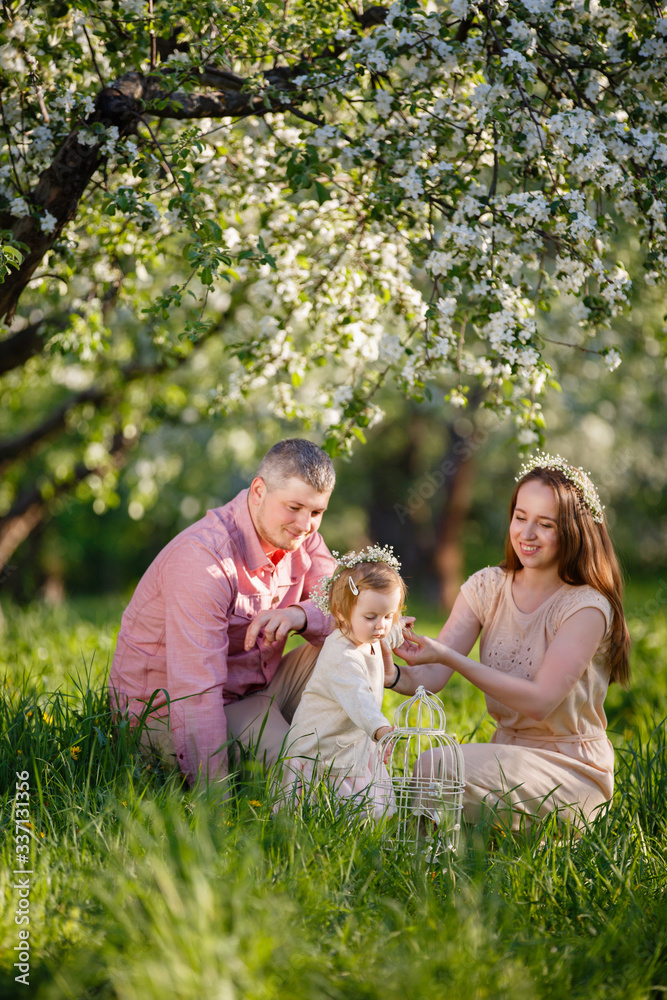Obraz premium little daughter with parents on a picnic in blooming apple garden. Mom loves her child. Spring story. Toddler girl with family in apple garden. Happy family in beautiful spring day. Tender relations