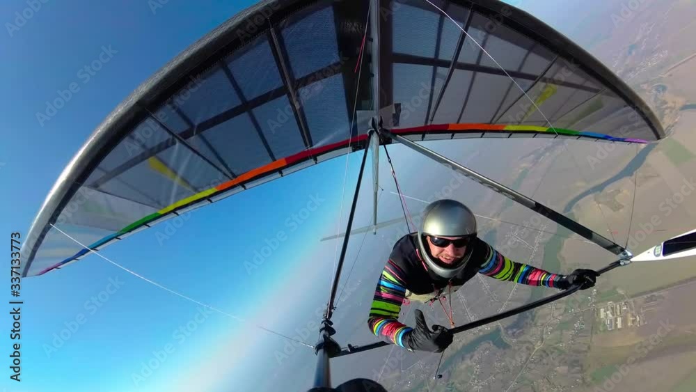 Smiling hang glider pilot shows thumb up while flyingh high above ground on his colorful wing