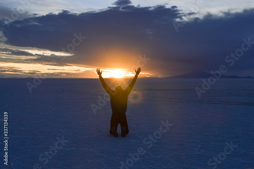 Man kneeling with raised arms at Salar de Uyuni in Bolivia at sunset time