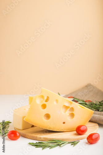 Various types of cheese with rosemary and tomatoes on wooden board on a white and orange background. Side view, copy space.