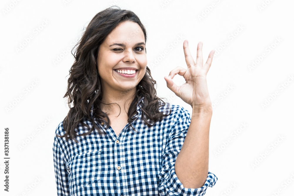 Joyful female customer making OK gesture, looking at camera, smiling. Young woman in casual checked shirt standing isolated over white background. Advertising concept Joyful female customer making OK gesture, looking at camera, smiling. Young woman in casual checked shirt standing isolated over white background. Advertising concept