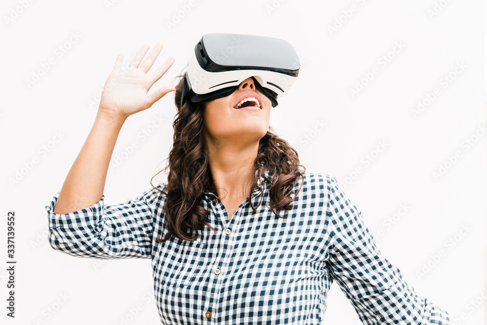 Positive excited female user in VR glasses enjoying experience. Young woman in virtual reality headset standing isolated over white background. VR game test concept Positive excited female user in VR glasses enjoying experience. Young woman in virtual reality headset standing isolated over white background. VR game test concept
