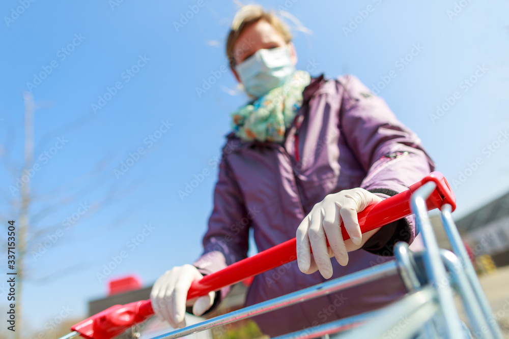 A german woman with a mouth protector and gloves on a shopping cart