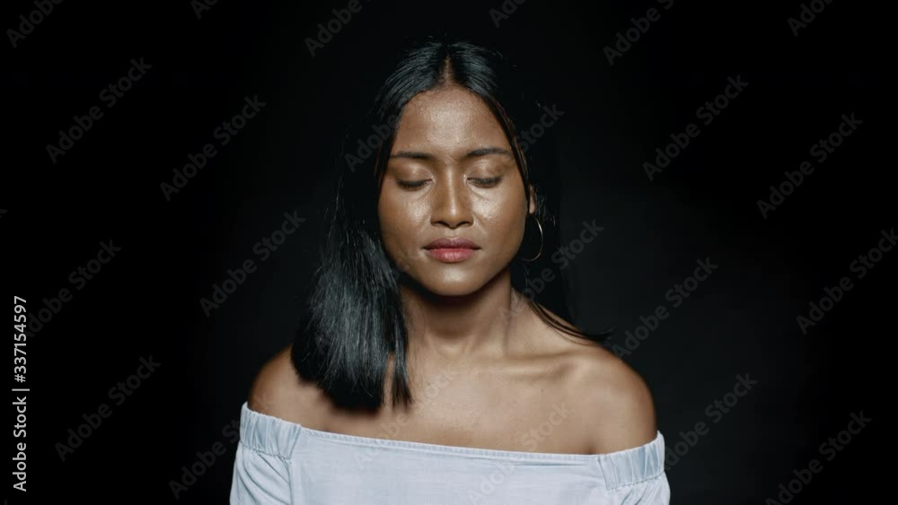 Close up of a young woman in jeans top on black background. Young dark skinned woman looking at camera.
