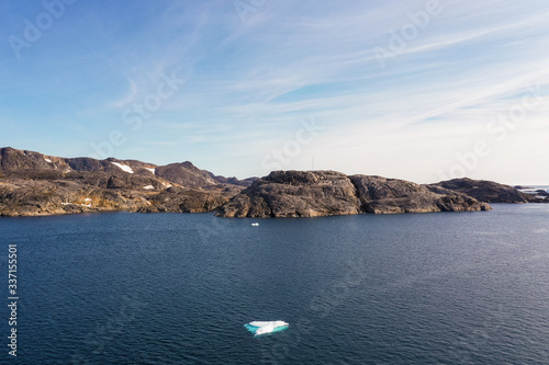 A Small Iceberg sits in front of a Greenlandic shoreline photo