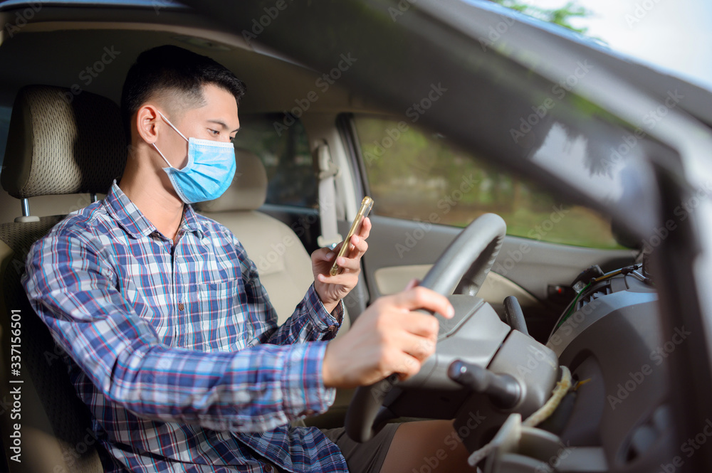 Man wearing a mask, press the mobile phone on the car. A man looking at the phone while driving.