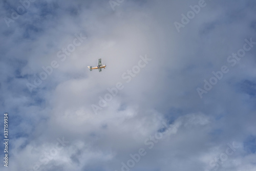 Small yellow-white plane in the clear sky with clouds.