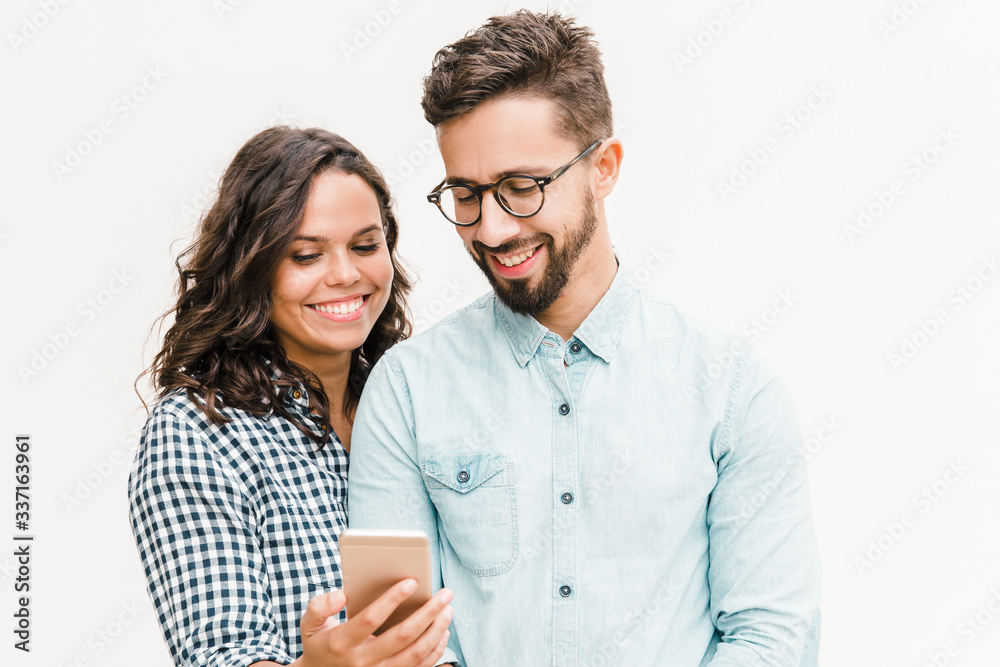 Happy cheerful woman showing message on phone to her boyfriend. Young woman in casual and man in glasses in glasses posing isolated over white background. Good news concept - obrazy, fototapety, plakaty 