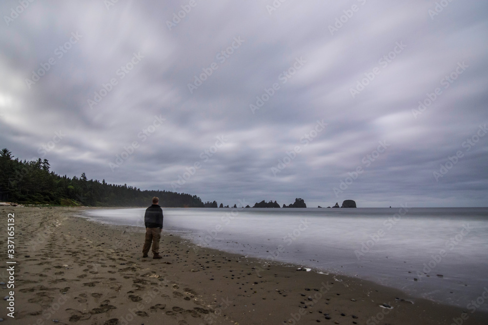 Adventurous man watching the ocean at a rugged Pacific Northwest beach at twilight.