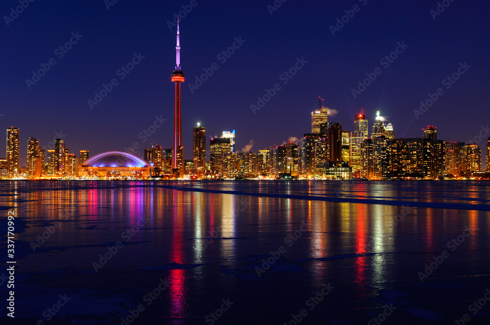 Toronto city skyline lights at night reflected on the frozen ice covered Lake Ontario