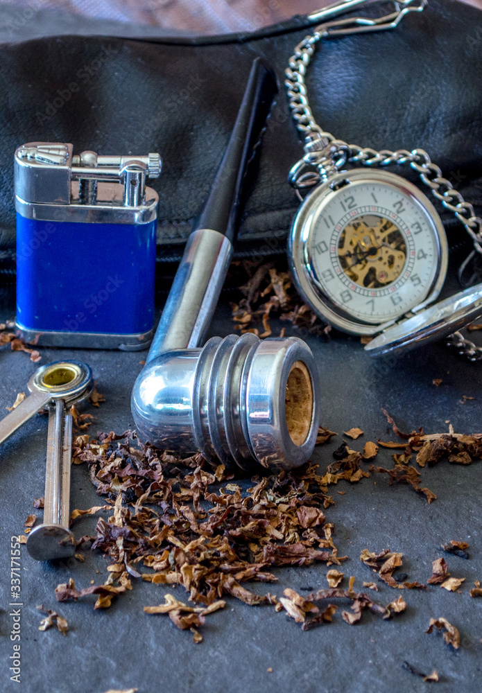 Aristicob pipe still life on slate background, with a flint lighter, tobacco and a silver pocket watch 