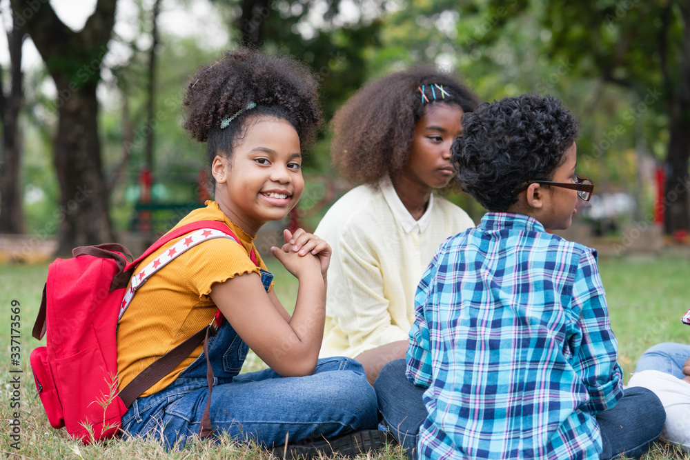 Portrait of cute little African with red backpacks and childrens sitting on the grass in the park, Education outdoor concept Portrait of cute little African with red backpacks and childrens sitting on the grass in the park, Education outdoor concept