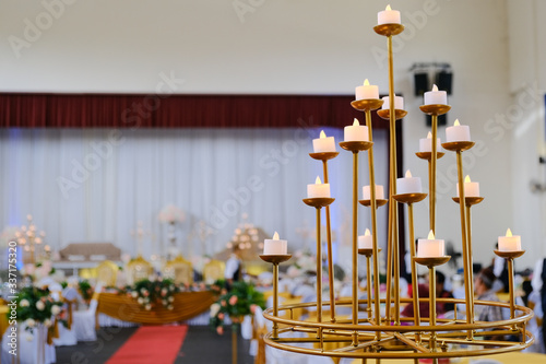 Pillar candles on golden multiple holder. Decorated event hall in background. Selective focus  photo