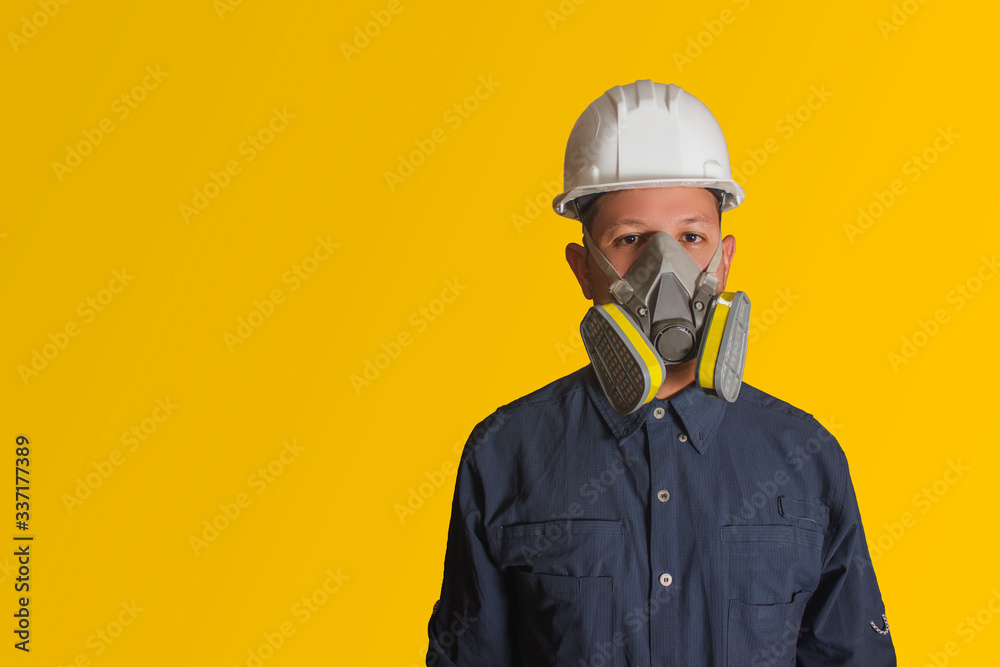 Hombre hispano con mascarilla y casco blanco de seguridad en fondo amarillo Hombre hispano con mascarilla y casco blanco de seguridad en fondo amarillo
