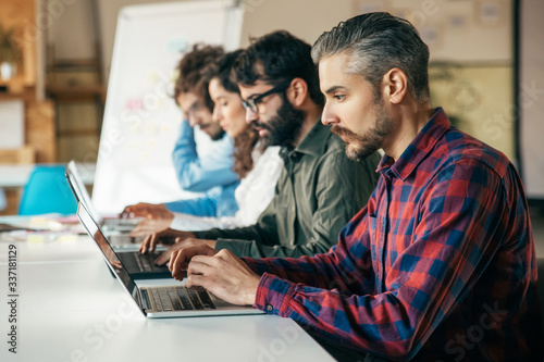 Startup team sitting at meeting table, using laptops. Business colleagues in casual working together in contemporary office space. Collaboration concept © Mangostar