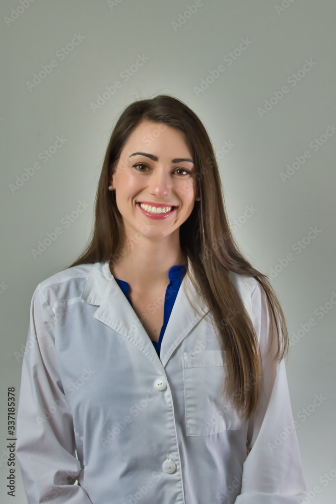 Woman healthcare professional in white coat isolated on grey wall. Head and shoulders visible. Woman healthcare professional in white coat isolated on grey wall. Head and shoulders visible.