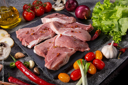 Raw pork steaks, fresh vegetables, spices close-up on a textured background